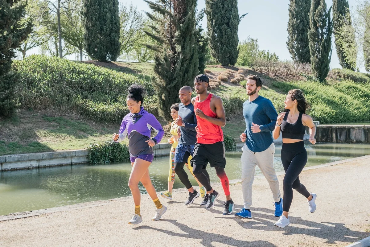Phone Addiction: Group of friends running together next to a lake