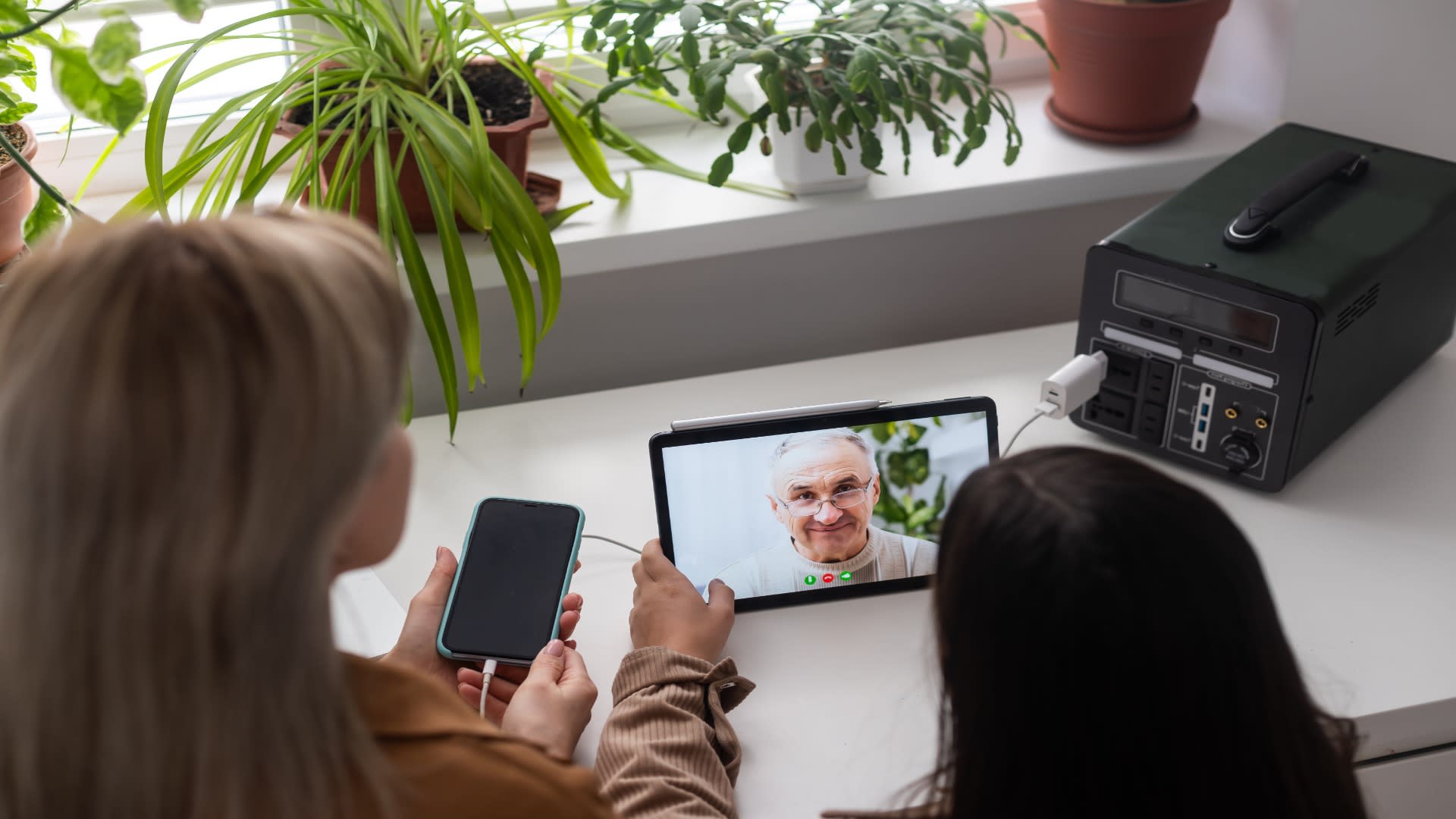 Mother and daughter using a tablet for a telepsychiatry call with an elderly man, highlighting family-based virtual mental health support.