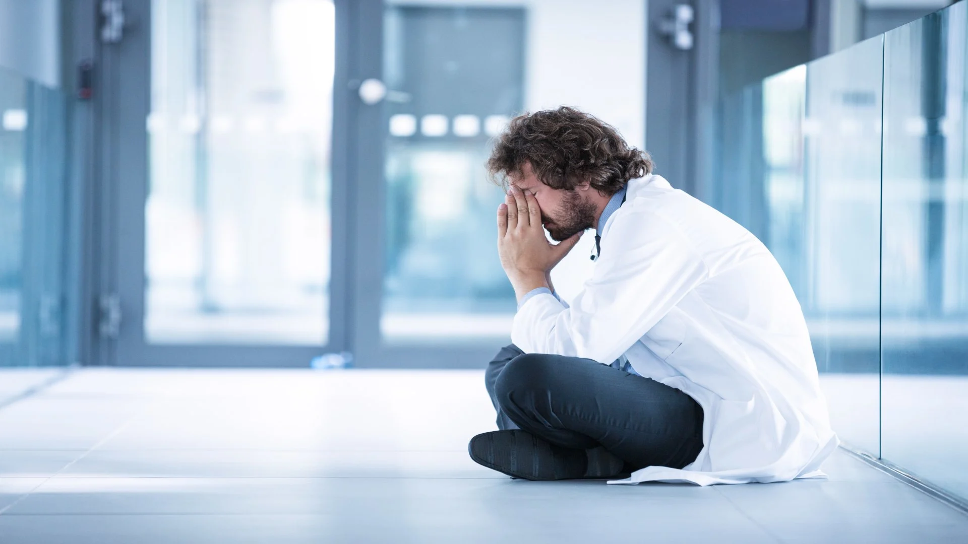 Healthcare professional sitting on the ground with his head in his hands, demonstrating that depression can affect anyone and highlighting why learning how to help someone with depression matters.