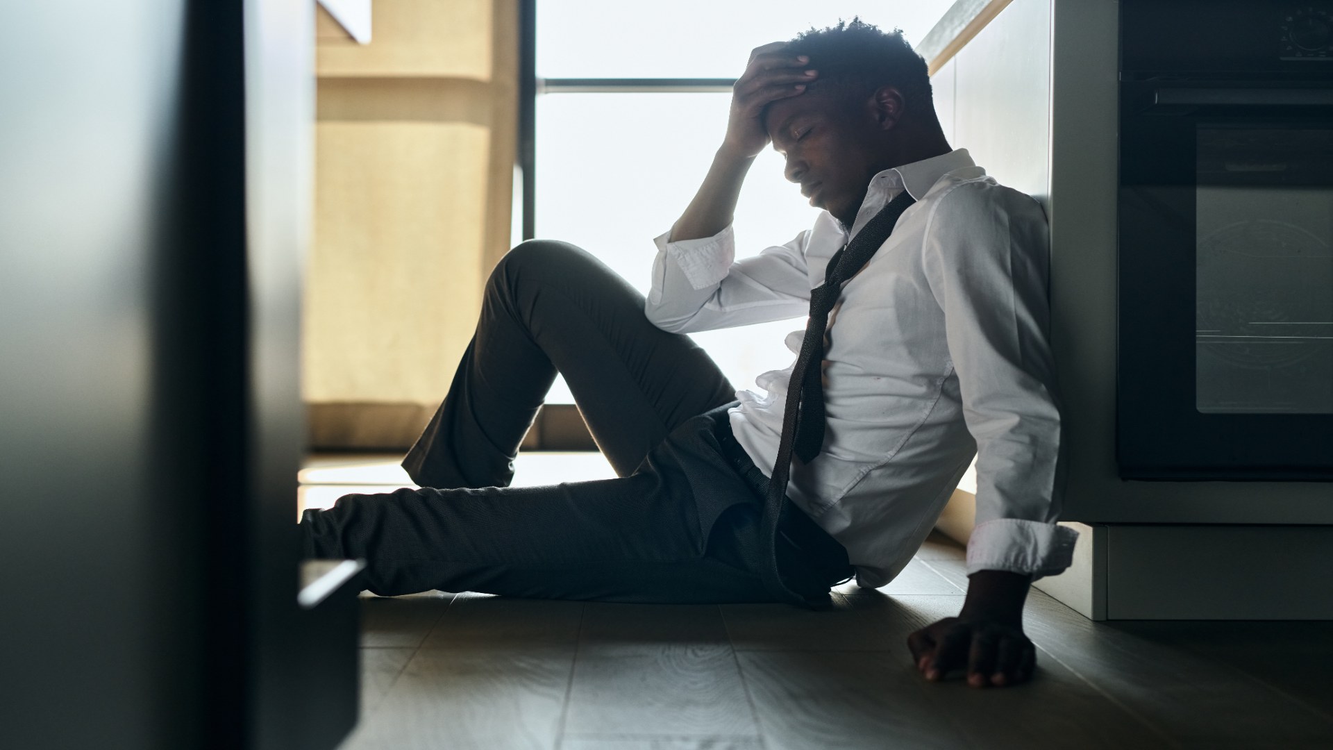Man in work clothes sitting on the floor with his head in his hand, showing signs of emotional exhaustion and the need to understand how to help someone with depression.