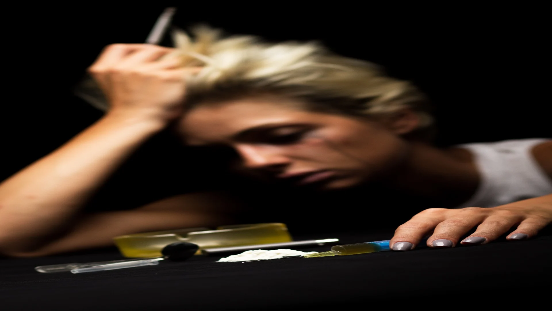 Young drug addict woman in a dark room struggling to feel normal shooting up speed.