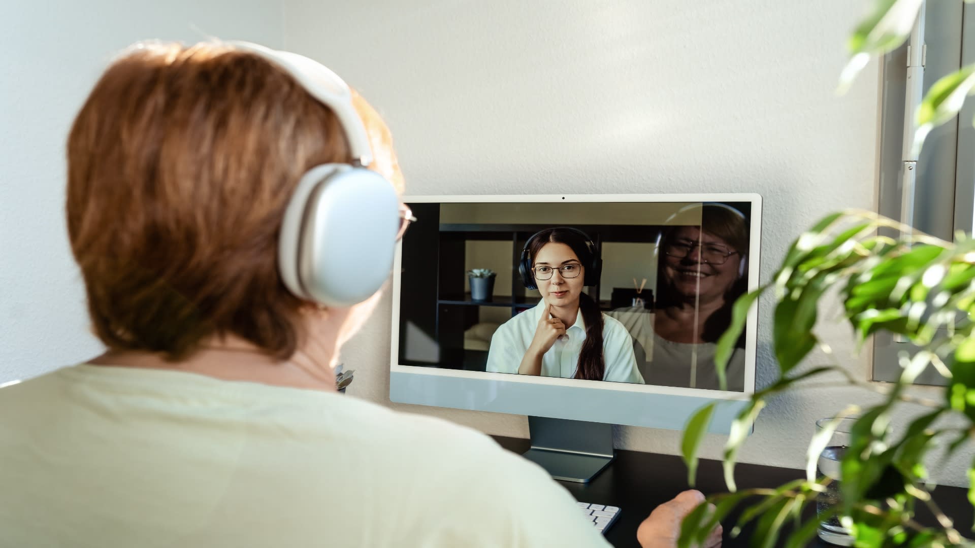 Senior woman wearing headphones during a telepsychiatry session, speaking with a female psychiatrist on a computer screen.