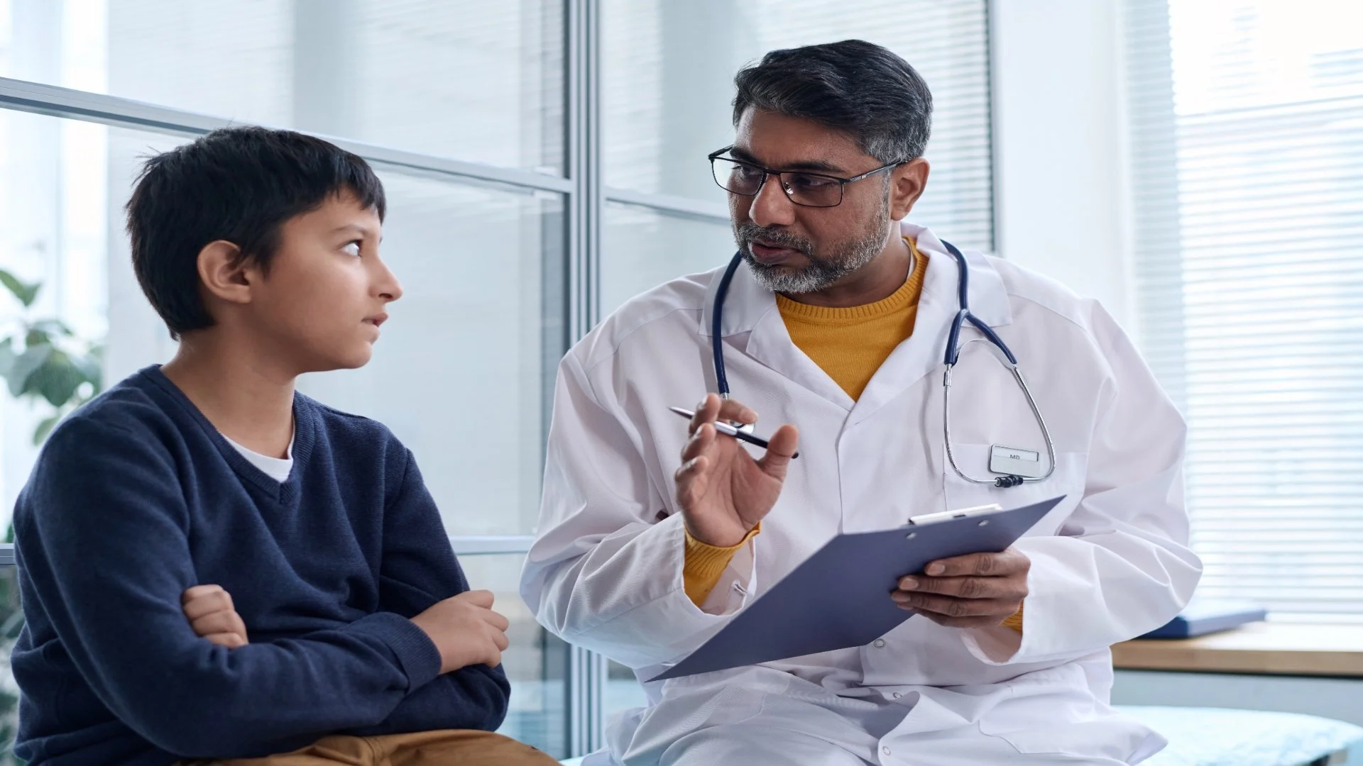 doctor-talking-to-boy-in-clinic-and-holding-clipbo-2025-03-18-22-13-20-utc