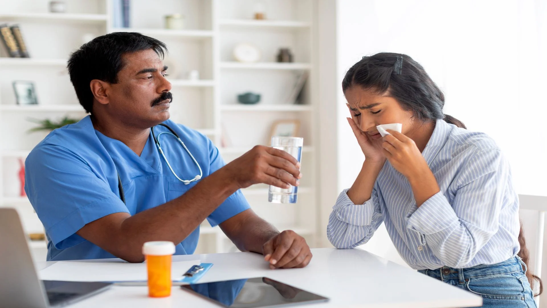 A concerned male doctor offers a glass of water to a crying young woman, highlighting the supportive care needed when managing oxycodone side effects like nausea, anxiety, or emotional distress.
