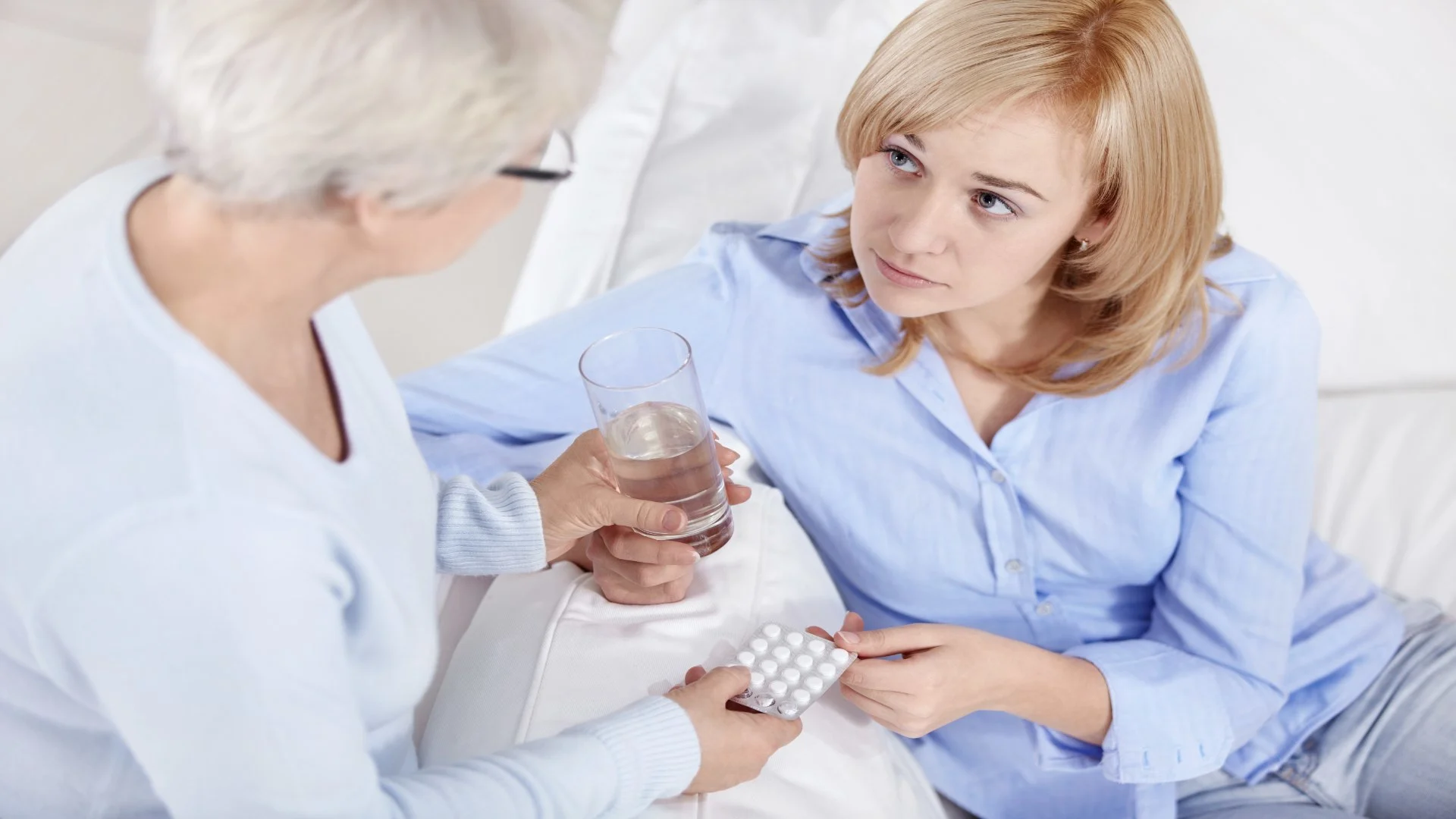 Concerned older woman offering pills and water to a younger woman, symbolizing care and stabilization after someone enters a k hole.
