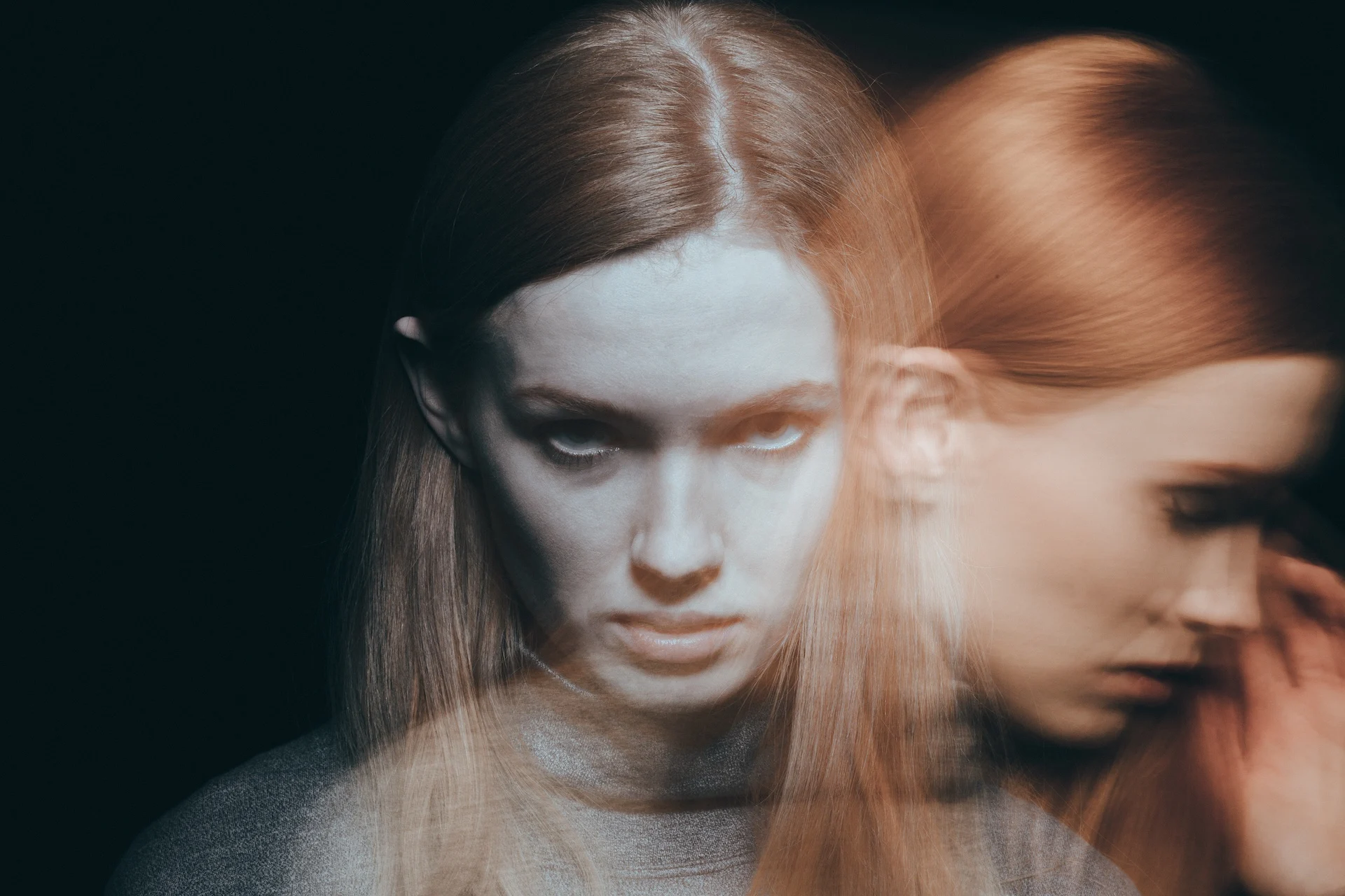 “Types of schizophrenia” – conceptual image of a young woman in dim light with a double-exposure effect, her face duplicated and blurred to suggest hallucinations, confusion, and intense emotional distress.