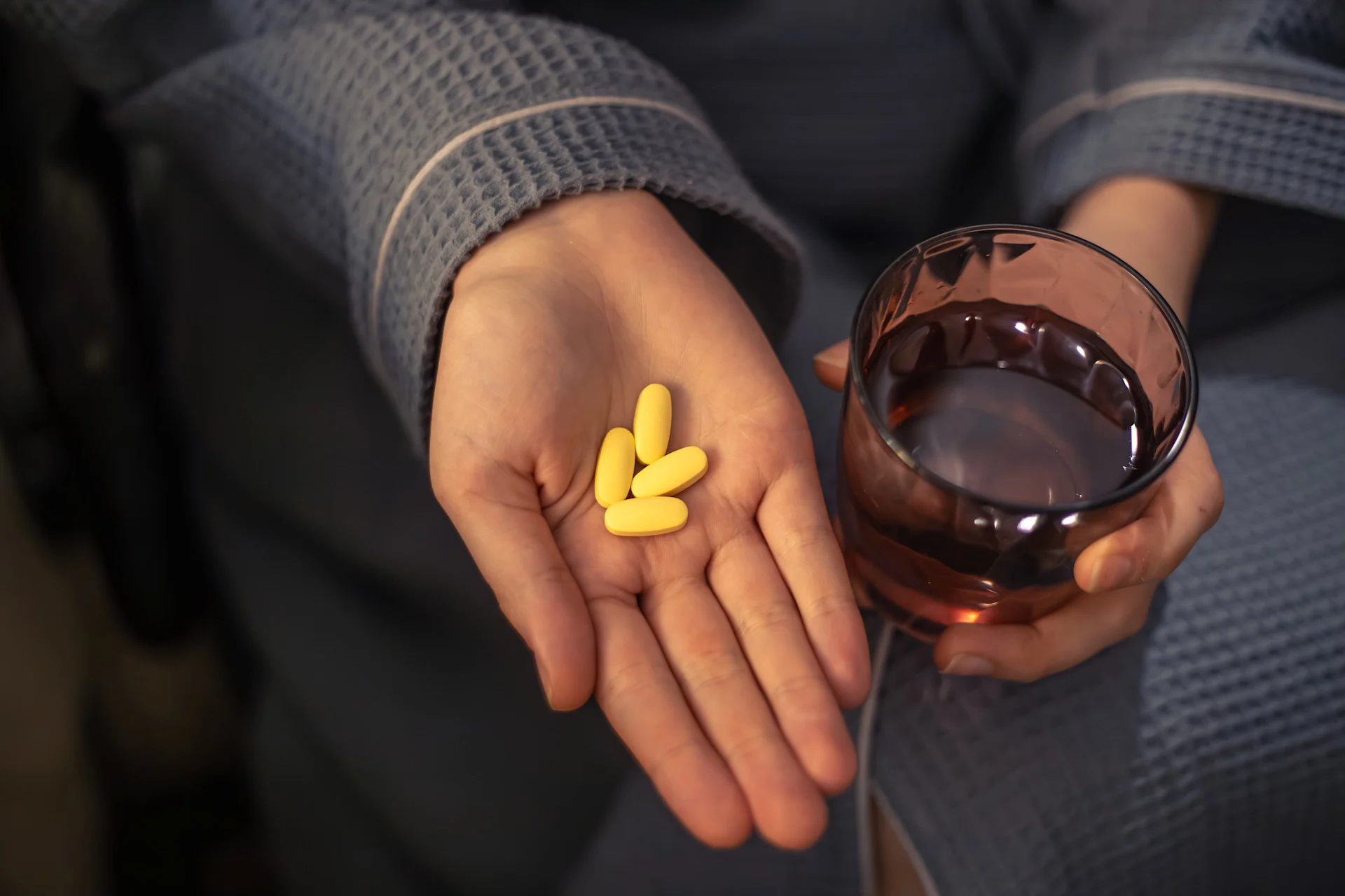 Zoloft and alcohol warning represented by a woman holding yellow pills and a drink, emphasizing the risks of mixing antidepressants with beverages.