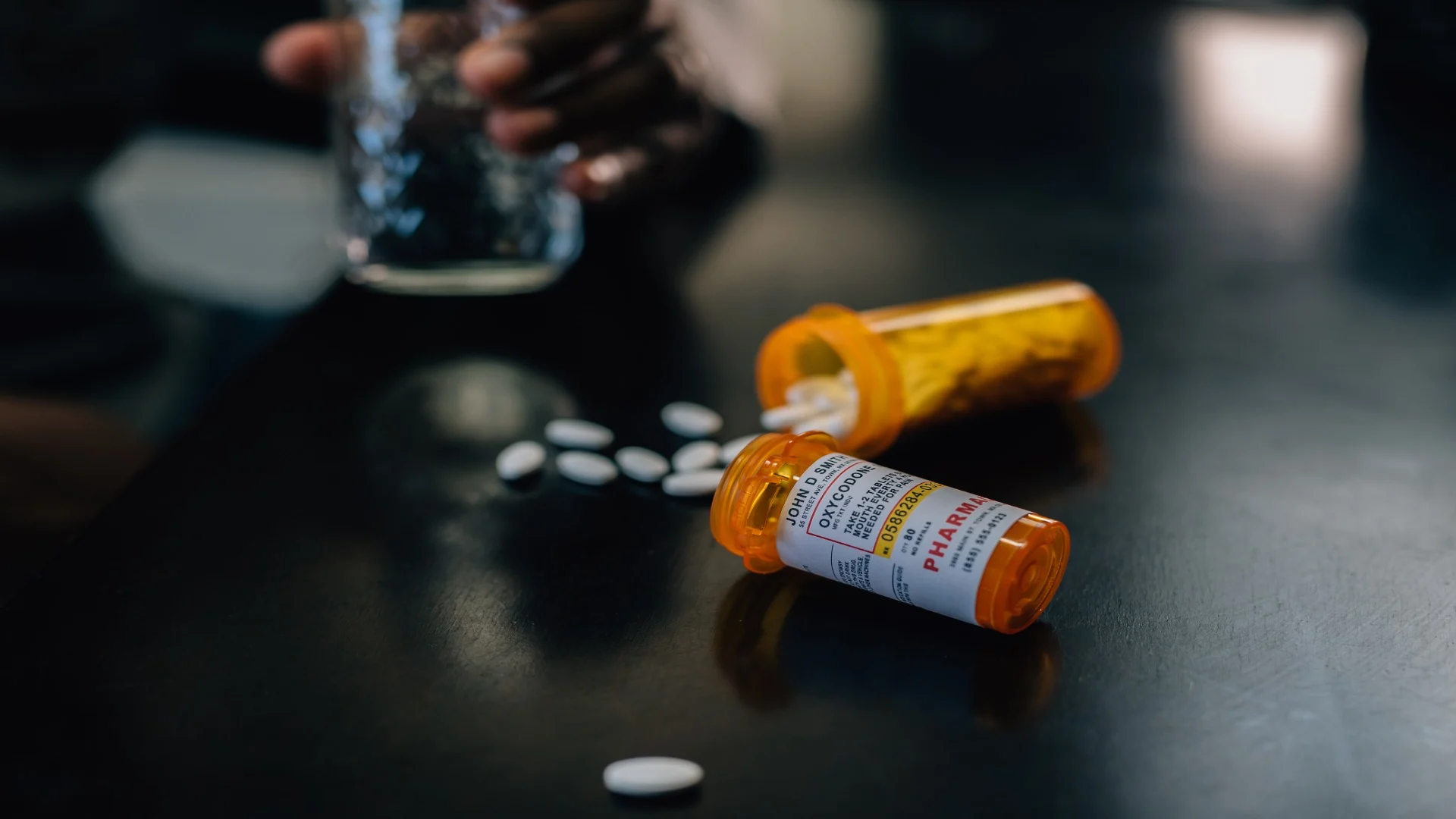 Opioid use disorder visualized by prescription pill bottles labeled oxycodone spilled across a dark table.