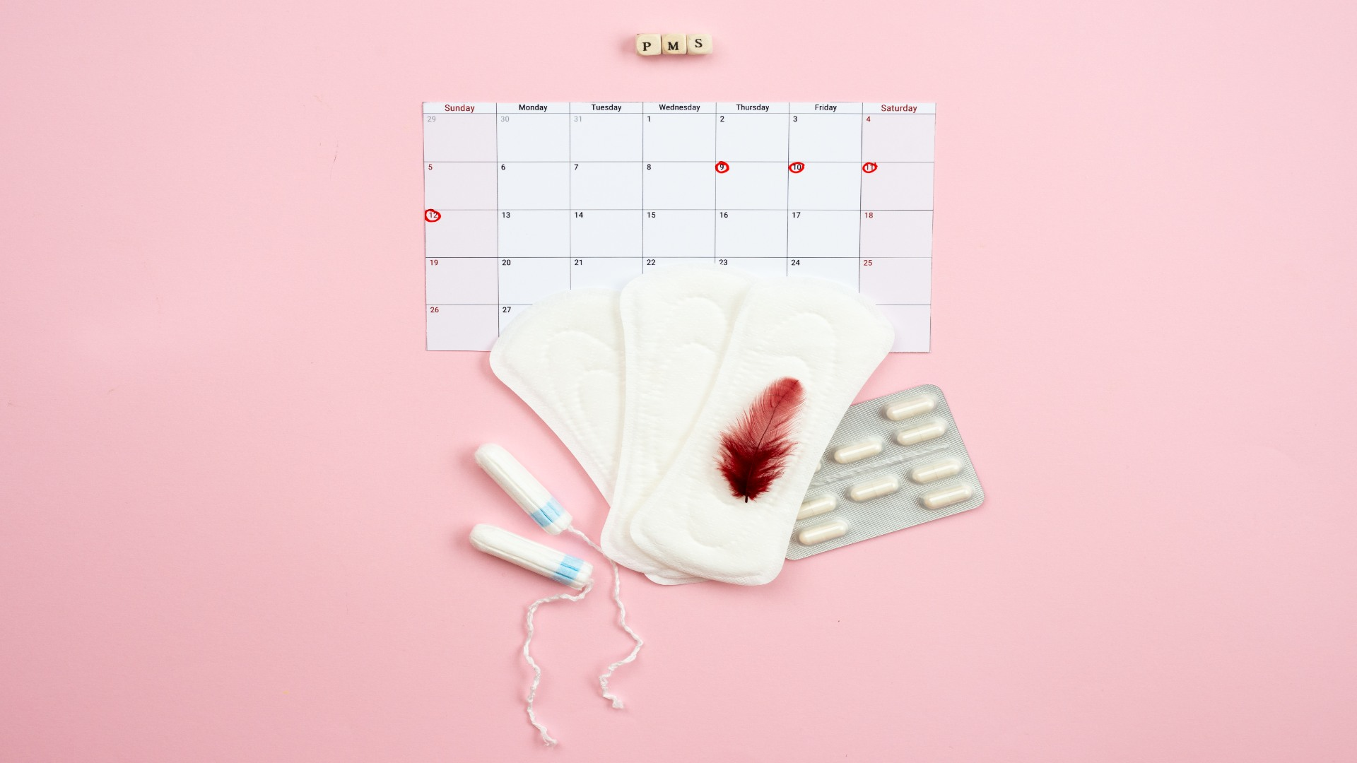 PMS calendar, sanitary pads, tampons, and feather stained with blood — representing menstrual symptoms and self-care essentials for PMDD management.