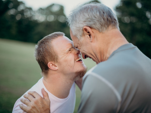 Down syndrome man and dad embracing one another smiling