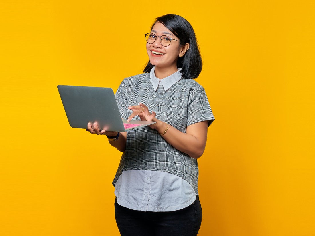 Employee happiness survey - Happy person stood with laptop on yellow background