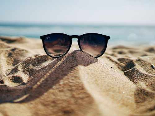 Sunglasses rested on mound of sand with sea in background