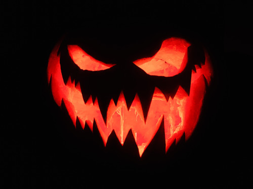 A carved out pumpkin in the dark with light shining through the gaps