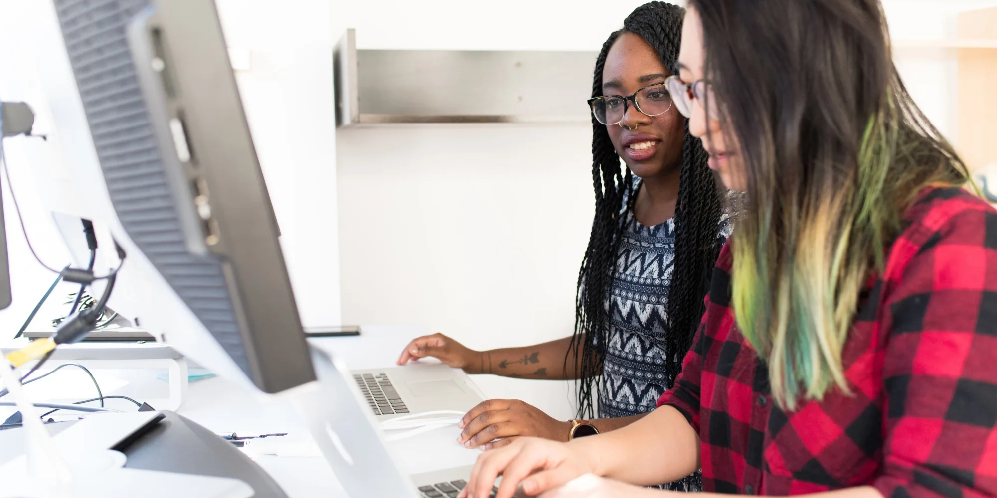 Two women standing at computers in discussion.