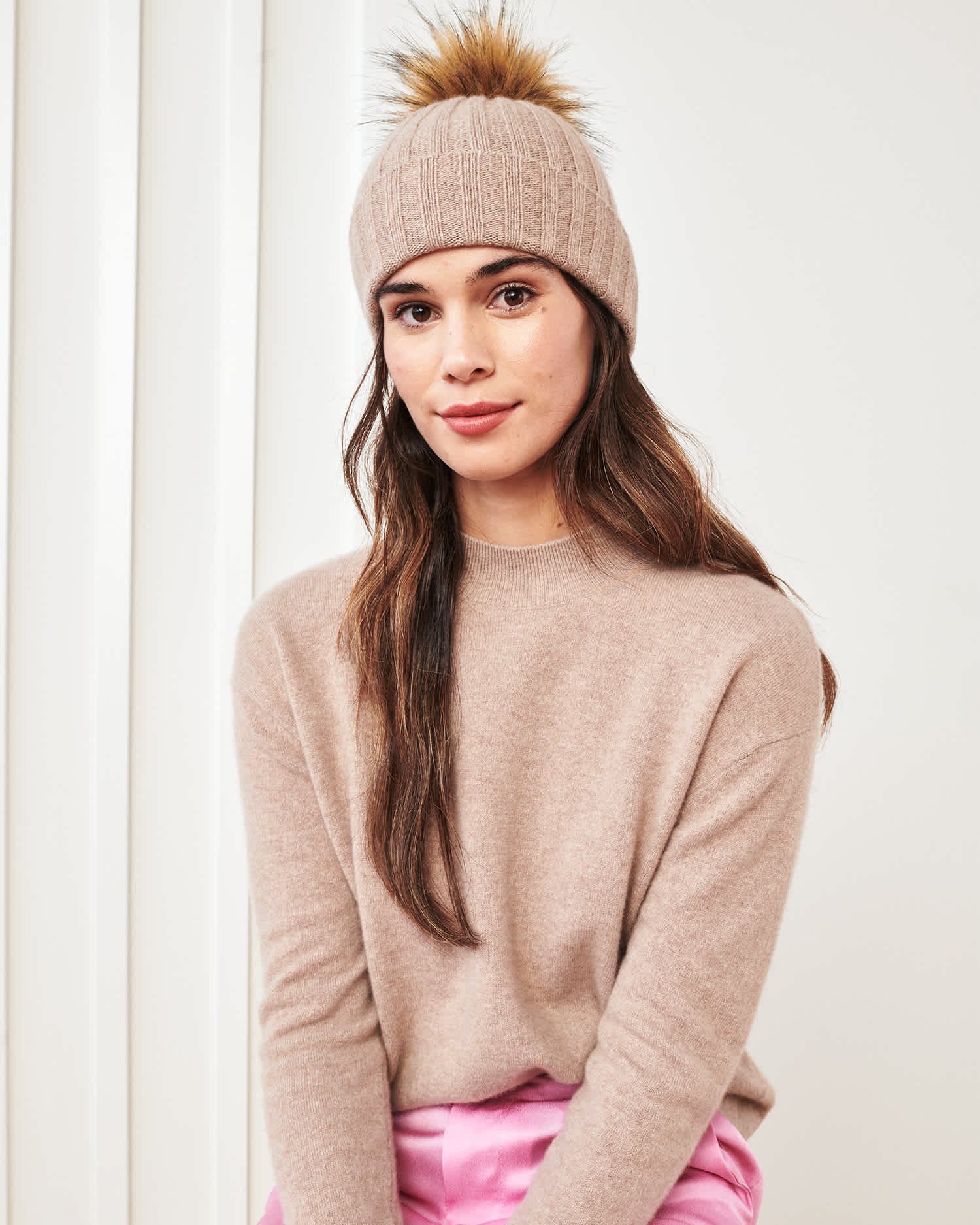 Woman wearing a cashmere pom pom beanie in oatmeal and matching cashmere mockneck sweater