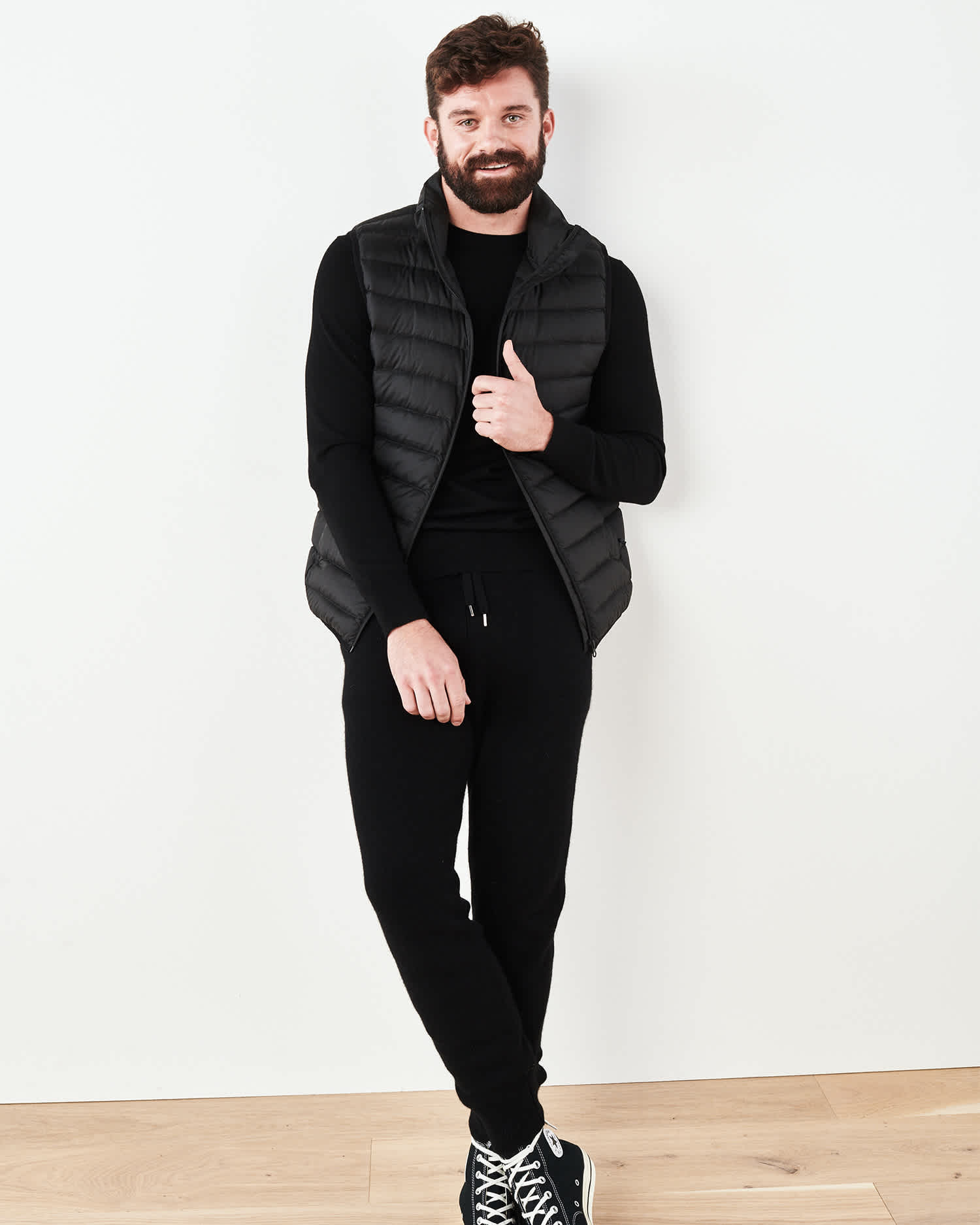 Man wearing cashmere men's cashmere joggers / cashmere sweatpants in black against the wall with a vest