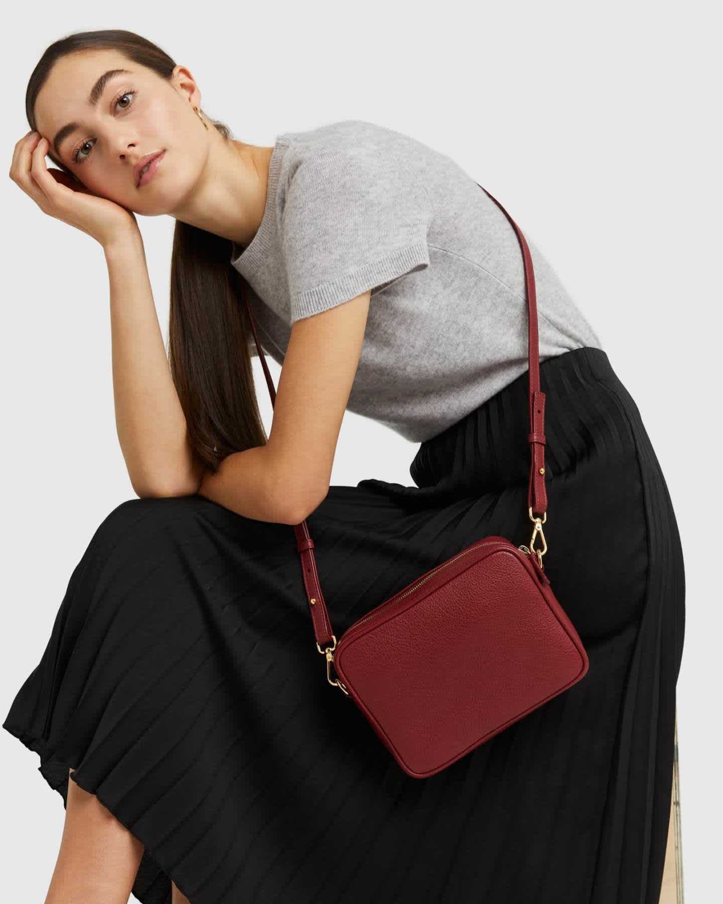 woman wearing Italian leather crossbody bag in red holding it