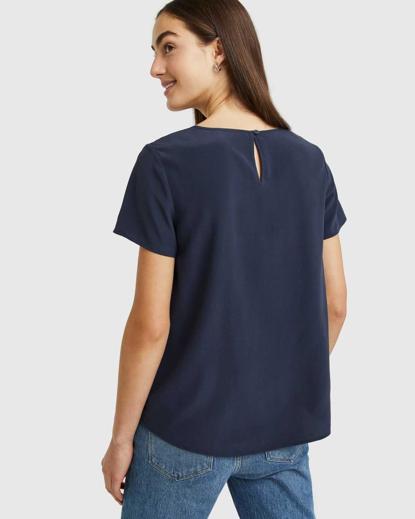 Woman wearing silk tee in navy from back smiling