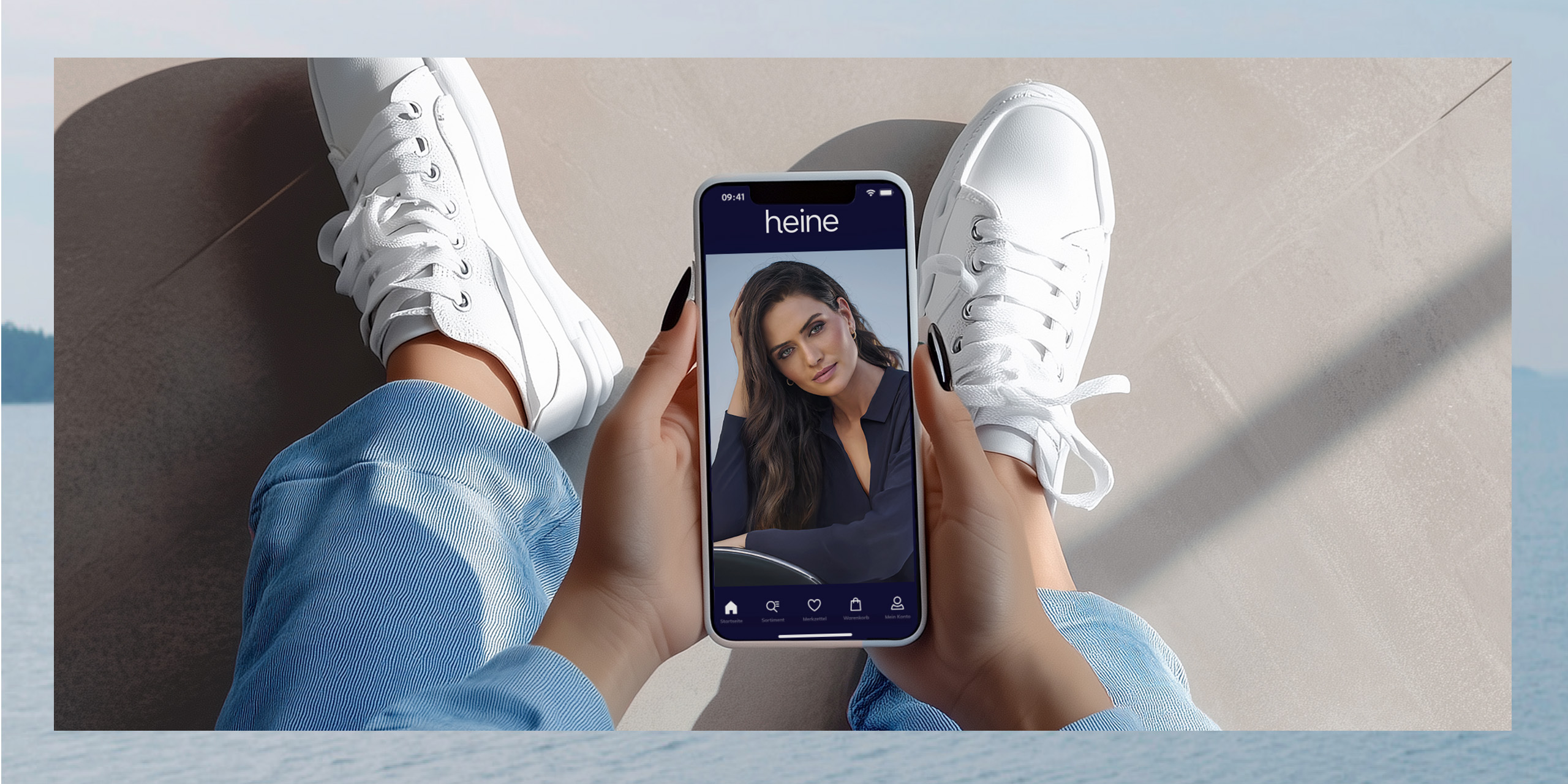 Ein Model sitzt mit weißen Sneakern und blauen Jeans, hält ein Smartphone mit heine-App, die ein Model zeigt.