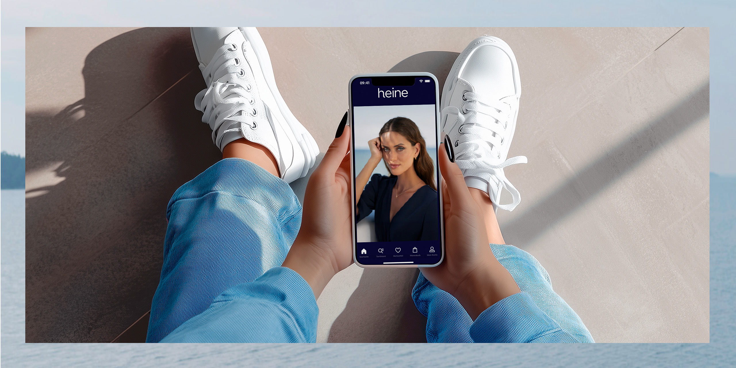 Ein Model sitzt mit weißen Sneakern und blauen Jeans, hält ein Smartphone mit heine-App, die ein Model zeigt.