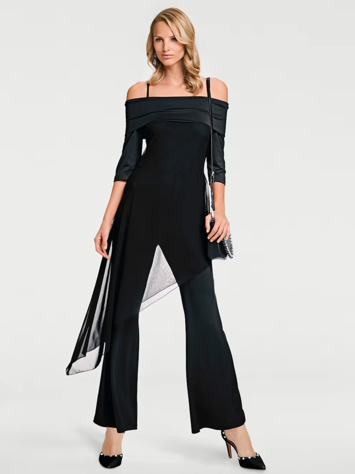 Eén model draagt een elegante zwarte jumpsuit met een asymmetrisch ontwerp en een off-the-shoulder snit. De look wordt afgemaakt met een inzetstuk van transparante stof en zwarte hoge hakken, die een stijlvolle en moEén model draagt een elegante zwarte jumpsuit met een asymmetrisch ontwerp en een off-the-shoulder snit. De look wordt afgemaakt met een inzetstuk van transparante stof en zwarte hoge hakken, die een stijlvolle en moderne indruk maken.derne indruk maken.
