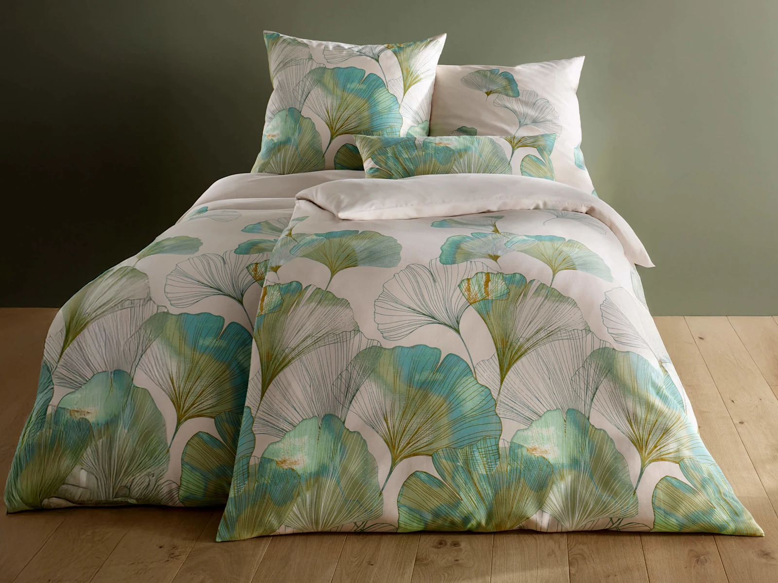 Tweepersoonsbed met beddengoed in groen- en blauwtinten, versierd met ginkgobladeren. De kamer heeft een houten vloer en groene muur.