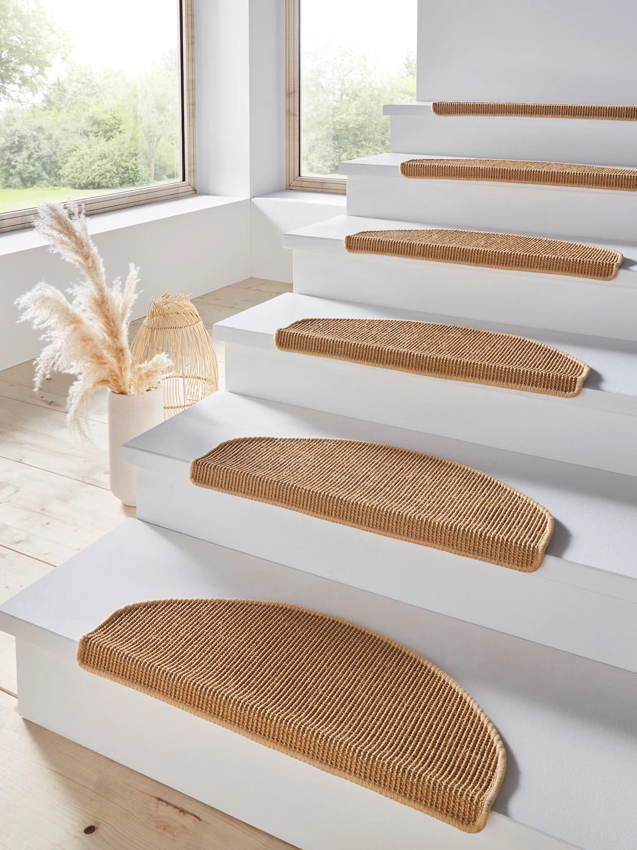 Un escalier blanc est équipé de marches semi-circulaires en moquette marron qui offrent un appui sûr. Une corbeille d'herbes décoratives se trouve dans un coin et la lumière du jour pénètre abondamment par la grande fenêtre.