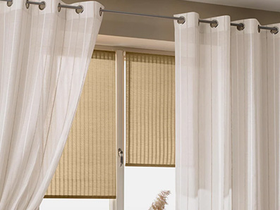 Rideaux blancs légers avec œillets métalliques devant une fenêtre équipée de stores beige.