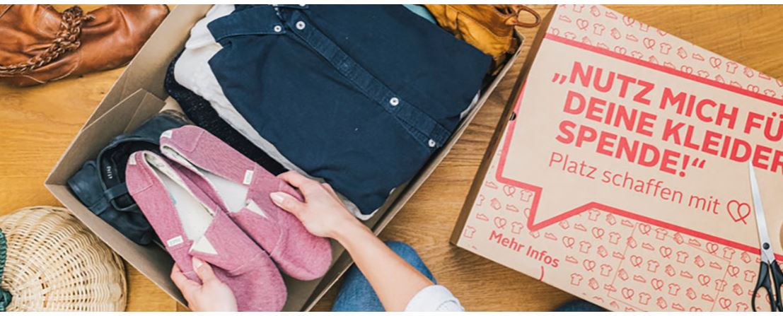 Kartons für Kleiderspenden mit Kleidung und Schuhen, daneben ein Karton mit der Aufschrift `Nutz mich für deine Kleiderspende! Platz schaffen mit Herz´.