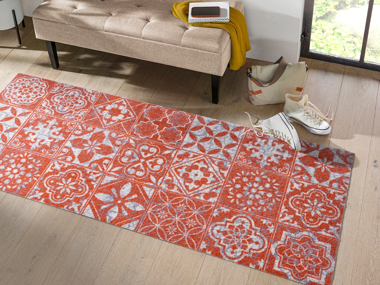Un tapis avec un motif orange et gris est posé devant une porte ouverte.