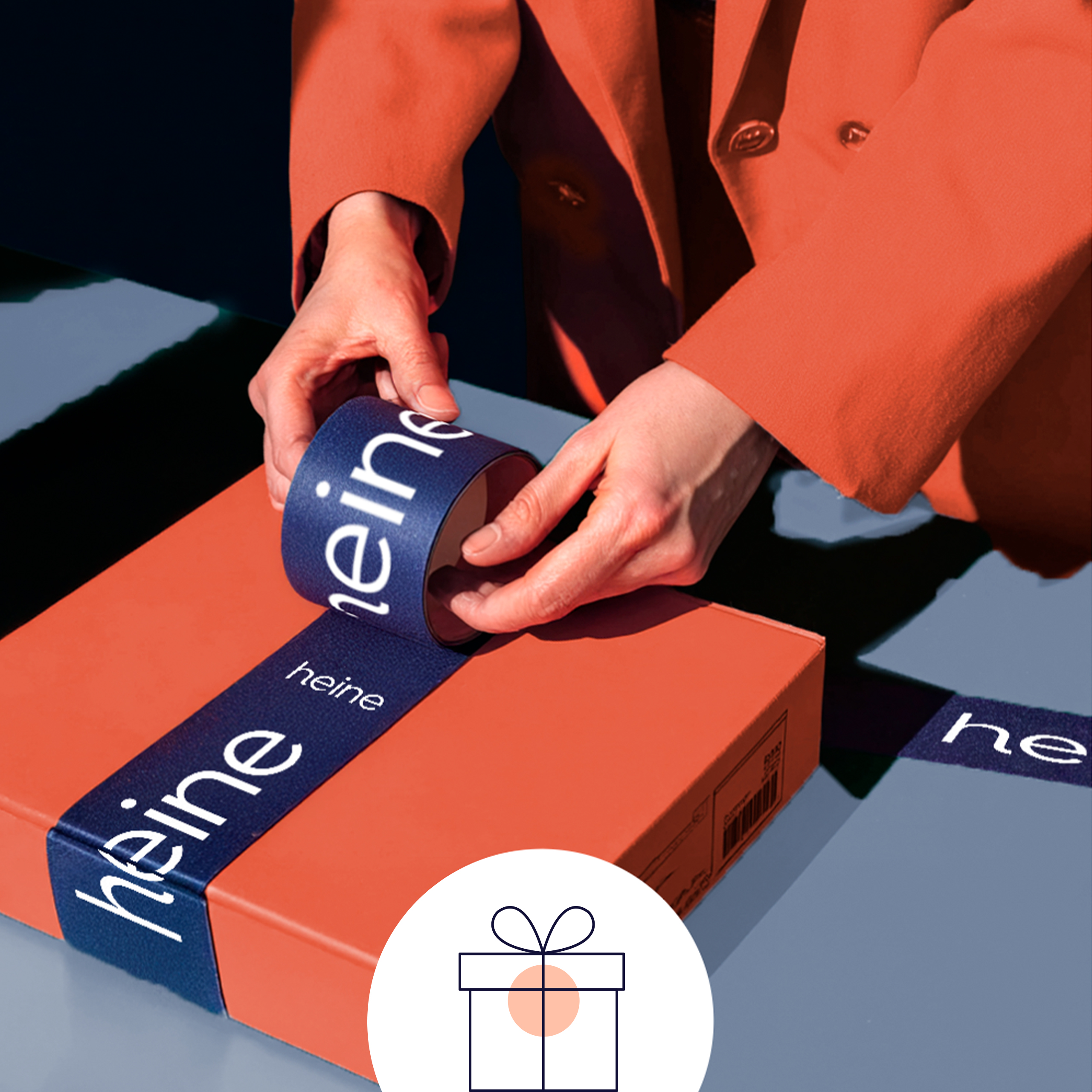 Ein Model verpackt ein orangefarbenes Paket mit dunkelblauem Band, auf dem 'heine' steht. Unten ist ein Geschenk-Symbol abgebildet.