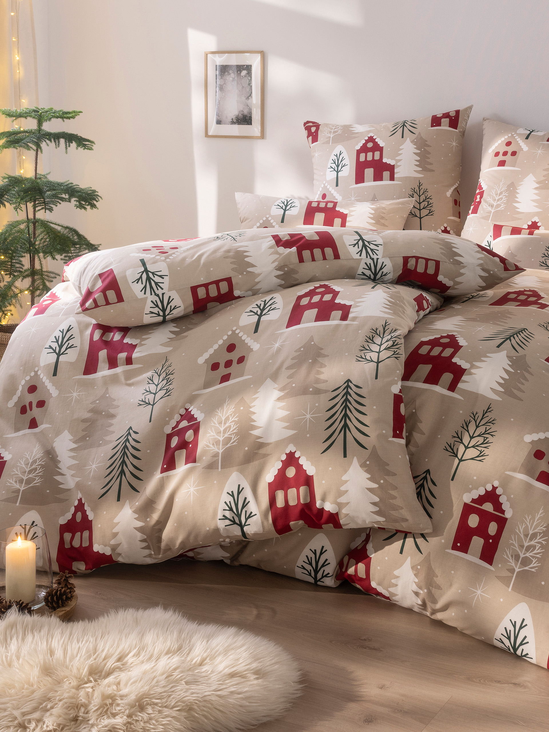 Bettwäsche mit winterlichem Muster aus roten Häusern, Tannenbäumen und Schneeflocken, dekoriert mit Kerzen und Tannenzapfen im Zimmer.