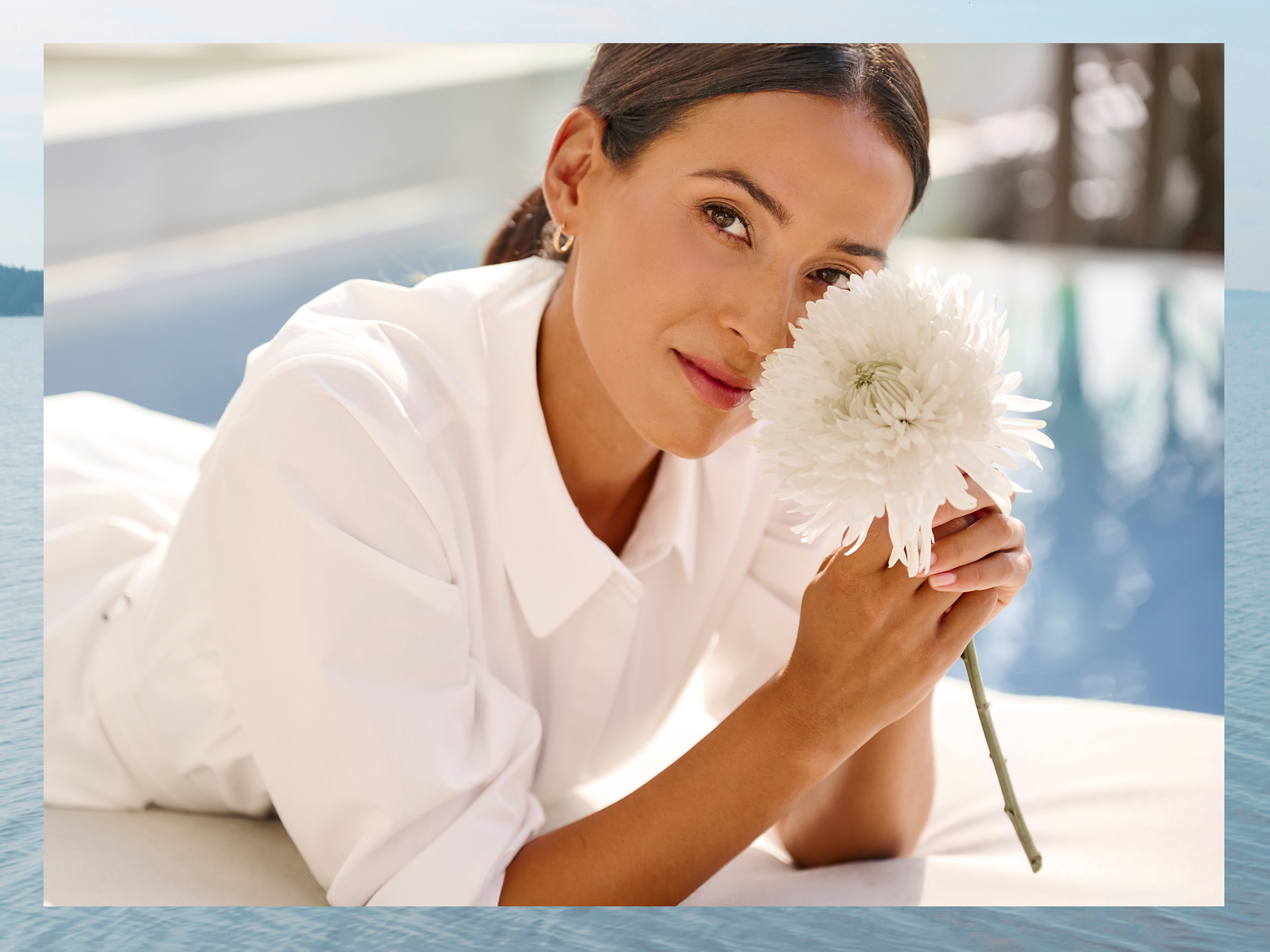 Une femme vêtue d'une robe blanche est allongée sur le ventre et tient une fleur blanche devant son visage.