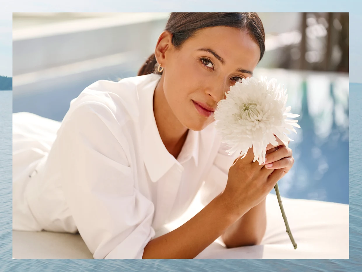 Vrouw in een witte jurk ligt op haar buik en houdt een witte bloem voor haar gezicht. Vrouw in een witte jurk ligt op haar buik en houdt een witte bloem voor haar gezicht.