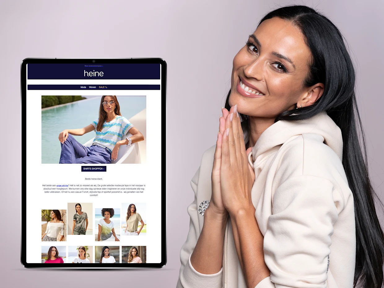 Tablet met een modewebsite van Heine op het scherm, gedragen door een persoon in een beige hoodie. Tablet met een modewebsite van Heine op het scherm, gedragen door een persoon in een beige hoodie.