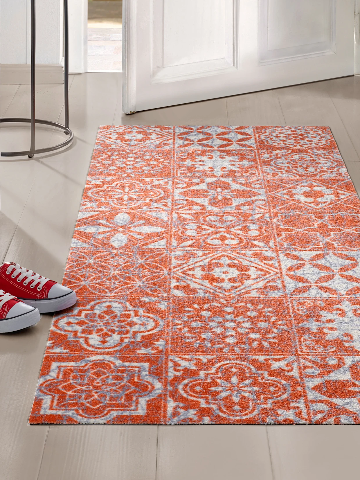 Een tapijt met een oranjegrijs patroon ligt voor een open deur.