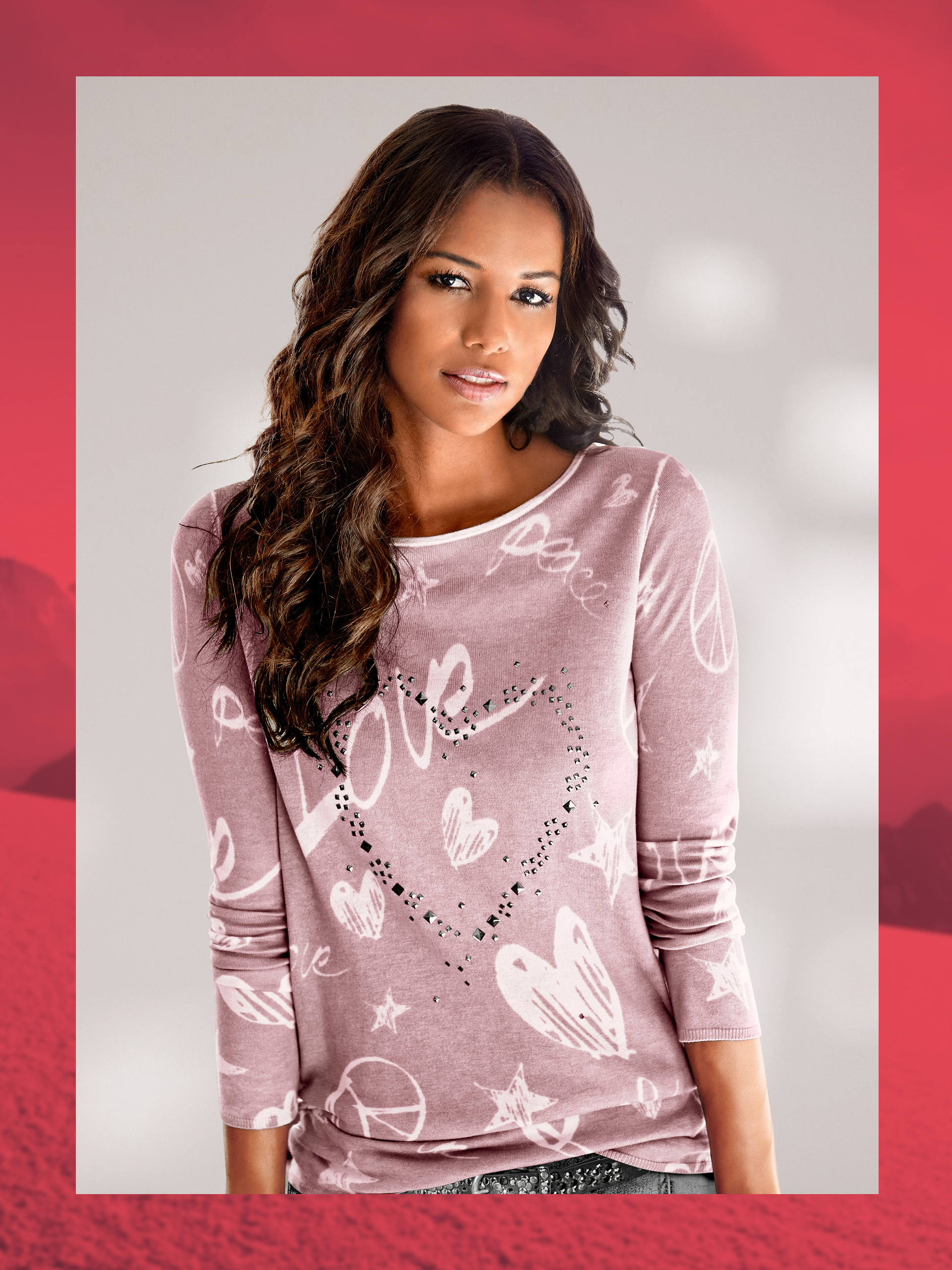 Ein Model trägt ein rosafarbenes Langarmshirt mit weißen Herz- und Sternmotiven vor neutralem Hintergrund.