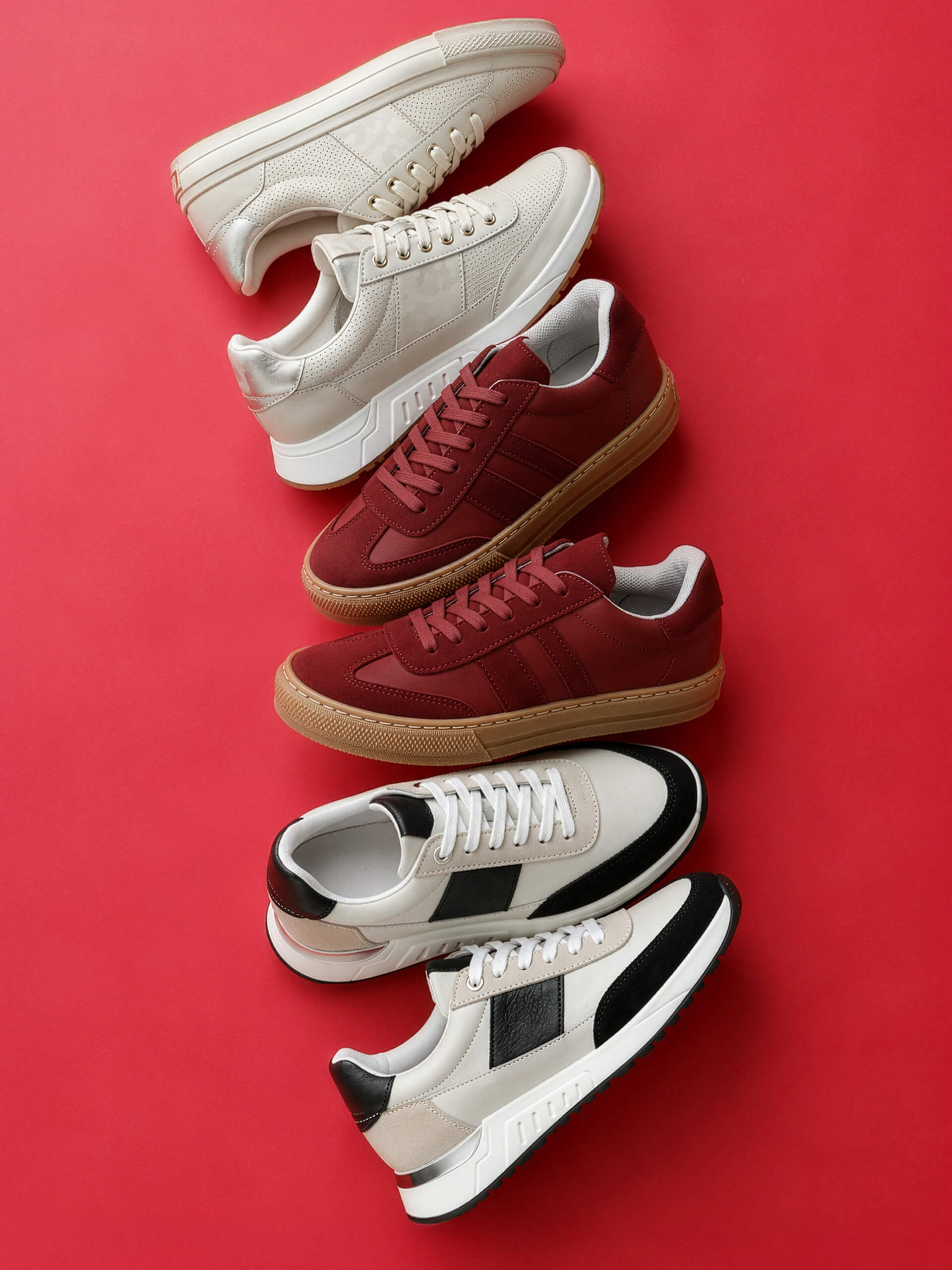 Drei Paar Sportschuhe in verschiedenen Farben: weiß, dunkelrot mit brauner Sohle und schwarz-weiß, auf rotem Hintergrund.