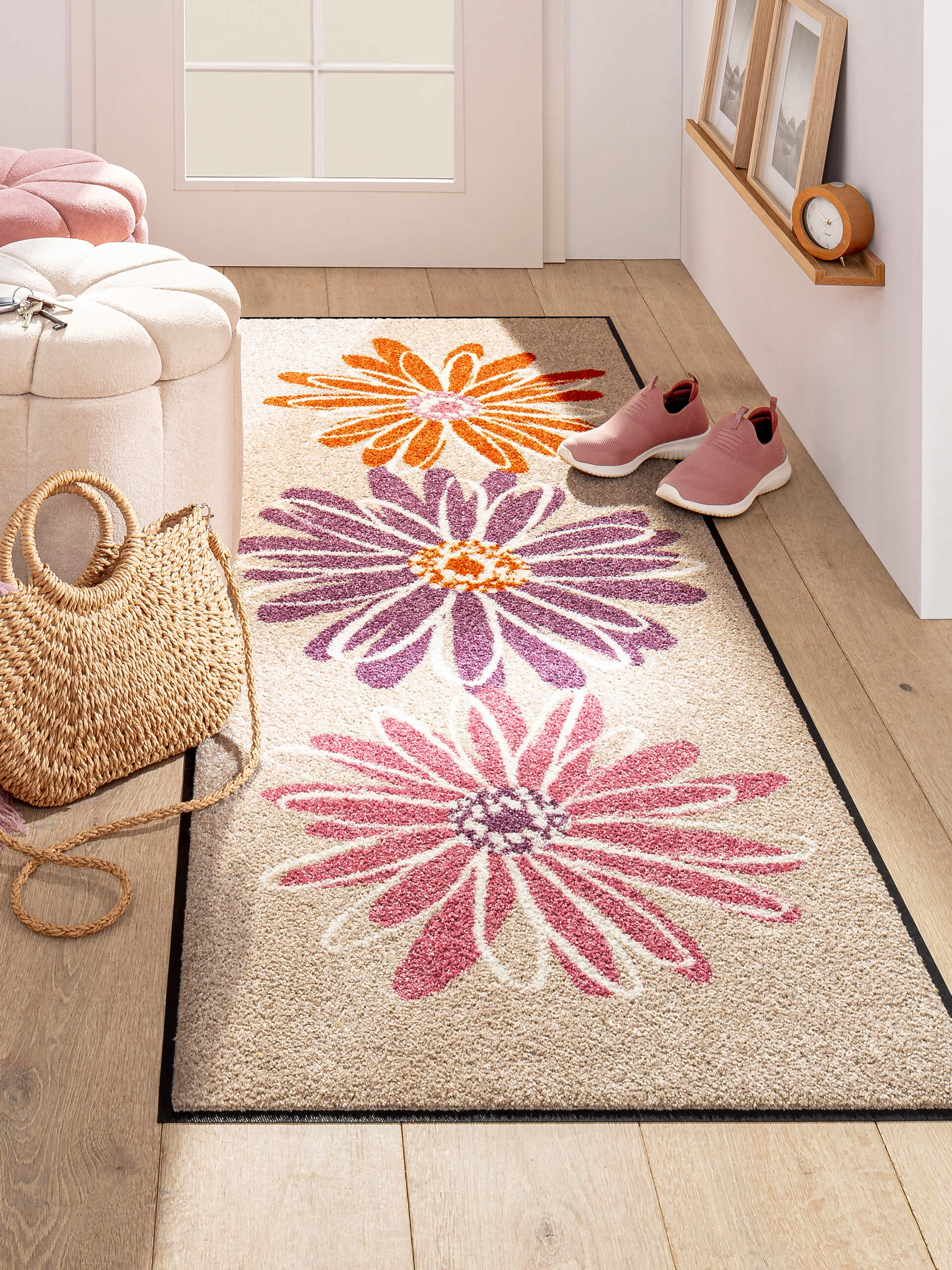 Heller Flur mit Läufer, der große Blumen in Orange, Lila und Pink zeigt. Daneben Korbtasche, rosa Schuhe und Sitzhocker.
