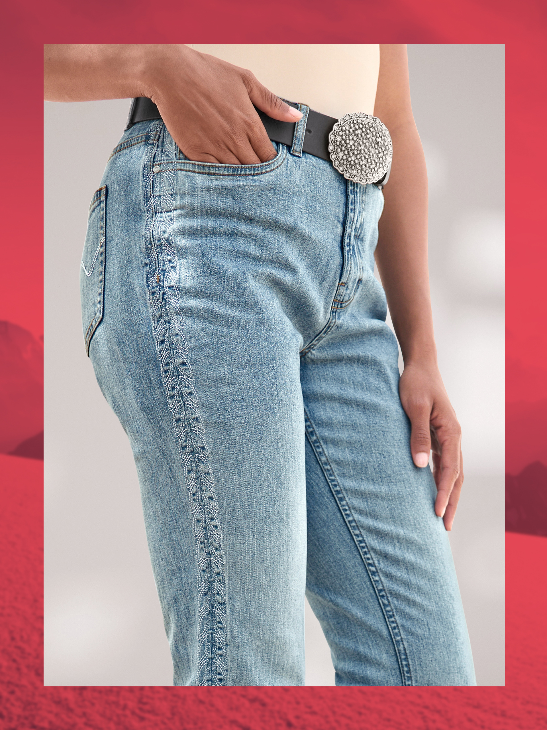 Een model draagt een lichtblauwe jeans met siernaad aan de zijkant en een zwarte riem met grote, glinsterende gesp.