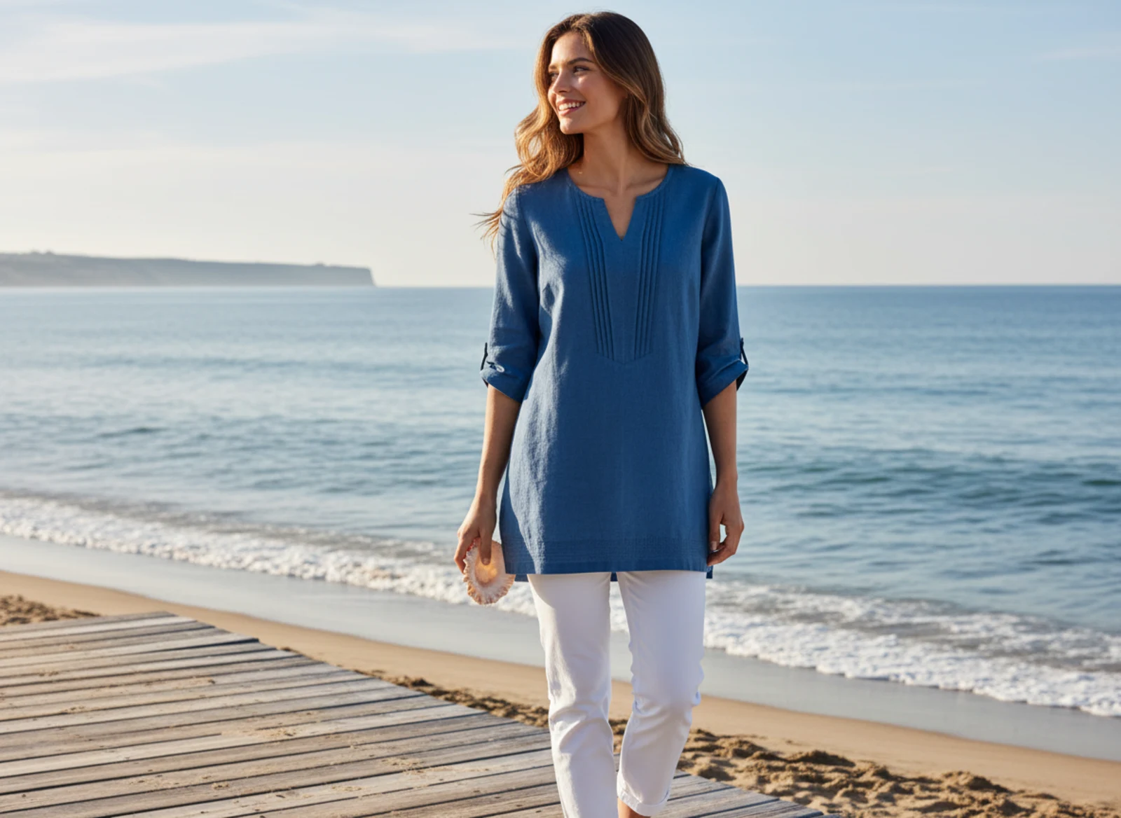 Frau in hellen Naturtönen auf einer Promenade mit weitem Blick aufs Meer Frau in hellen Naturtönen auf einer Promenade mit weitem Blick aufs Meer
