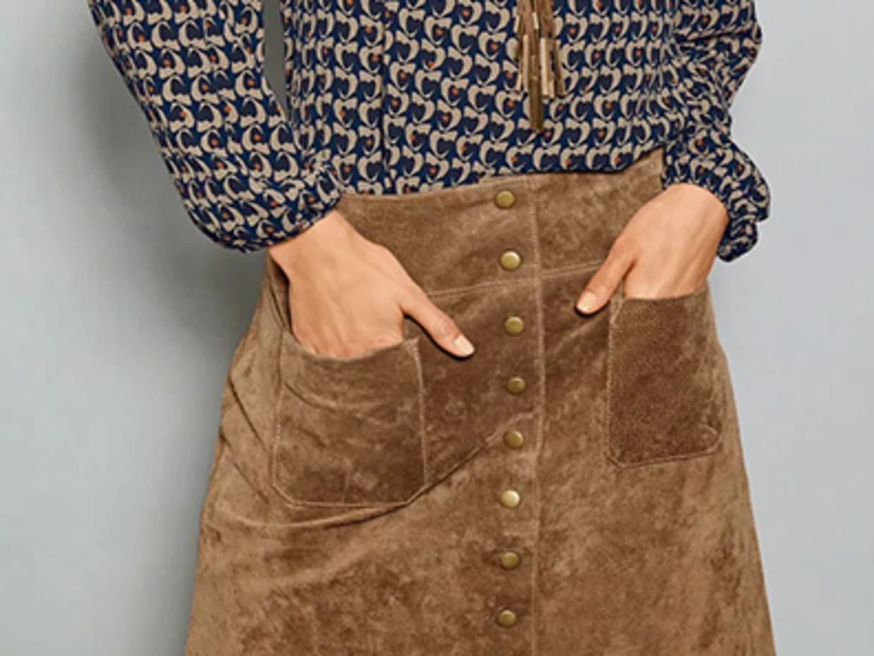 Chemisier à motifs bleu et beige associé à une jupe en daim marron avec boutons et poches.