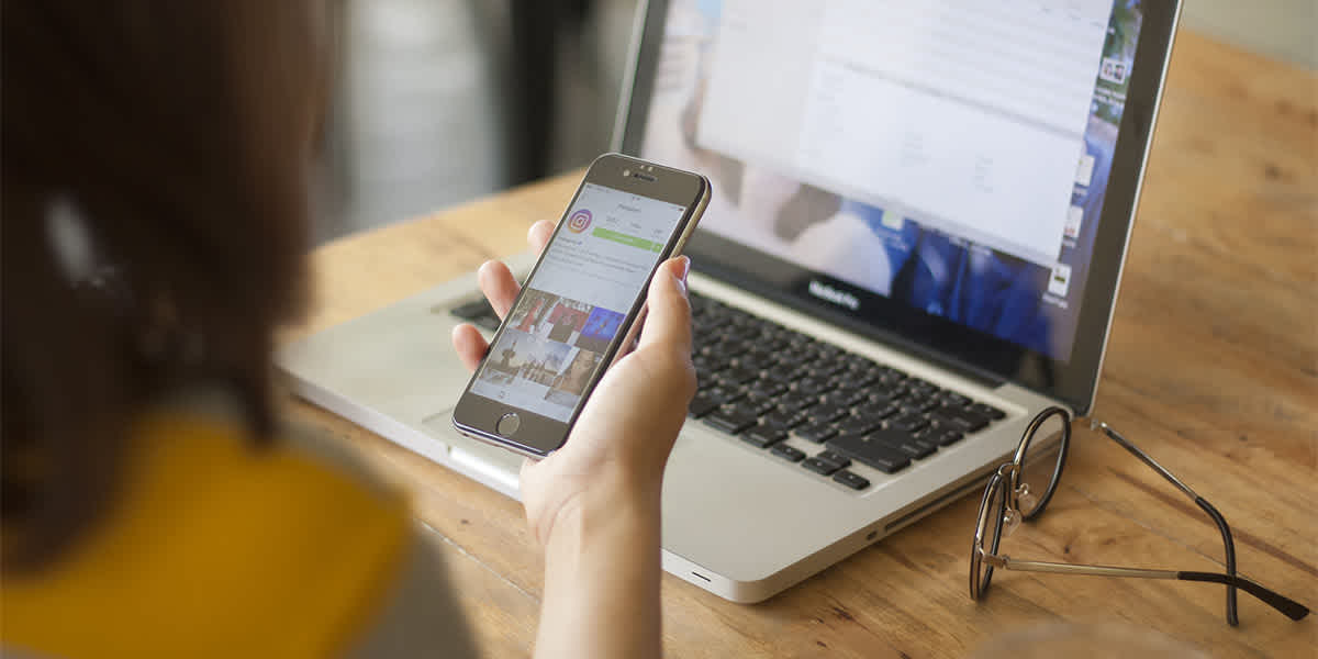 Női vállalkozó Instagram vállalkozói fiókot kezel okostelefonon egy laptop előtt ülve