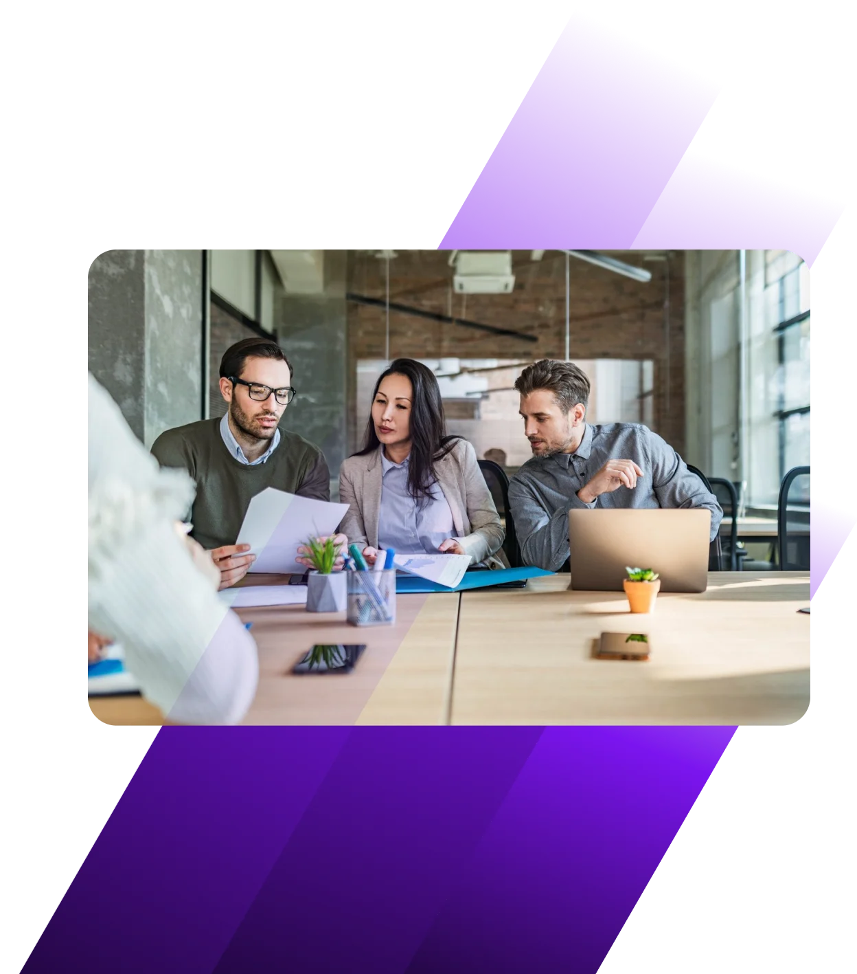 Three professionals collaborating at a modern office table with documents and laptop in an industrial-style workspace.