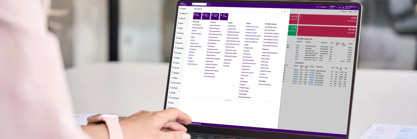 Person using laptop displaying business dashboard with purple navigation menu and data tables showing financial figures.