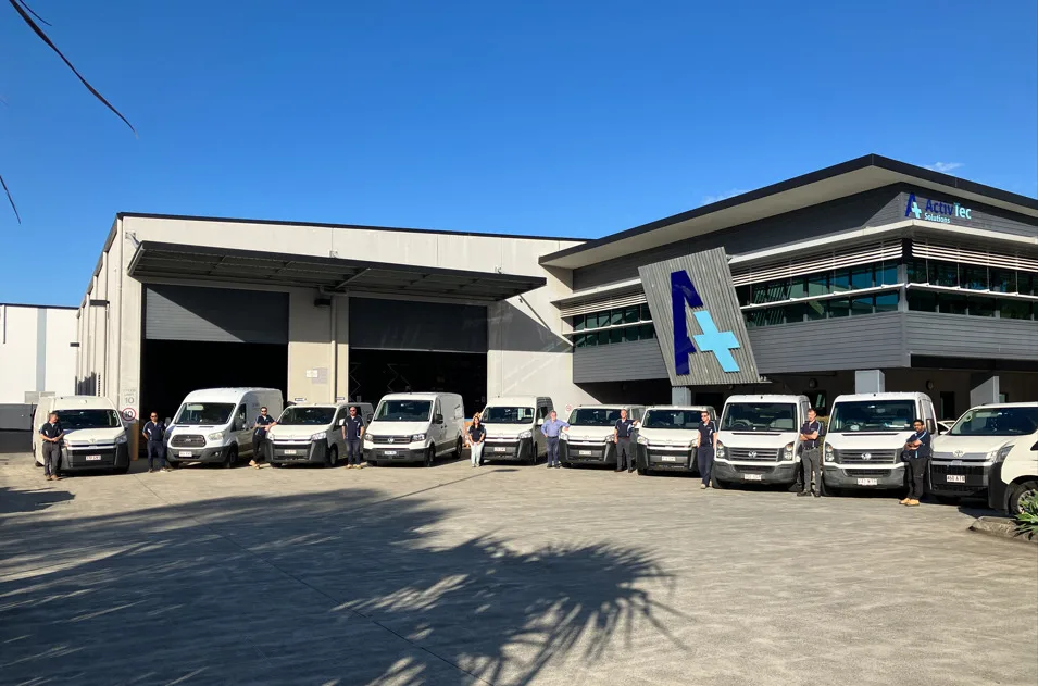 Fleet of white service vans lined up outside a commercial building with Activ-Tec logo under clear blue sky.