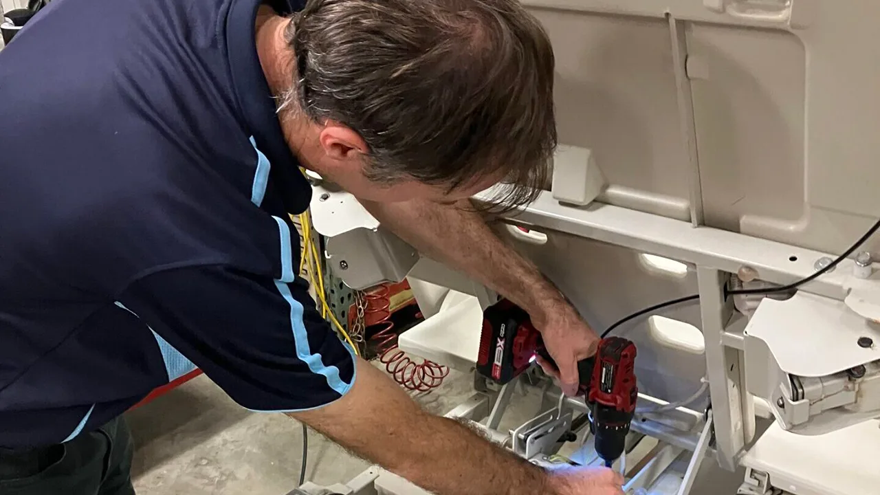 Person in navy uniform using red power drill to repair or install medical equipment components in a hospital setting.
