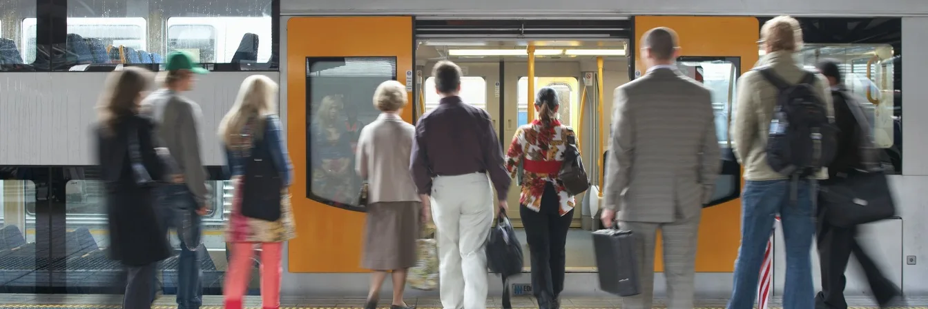 Passengers boarding and exiting a yellow and gray train at a station platform during rush hour.