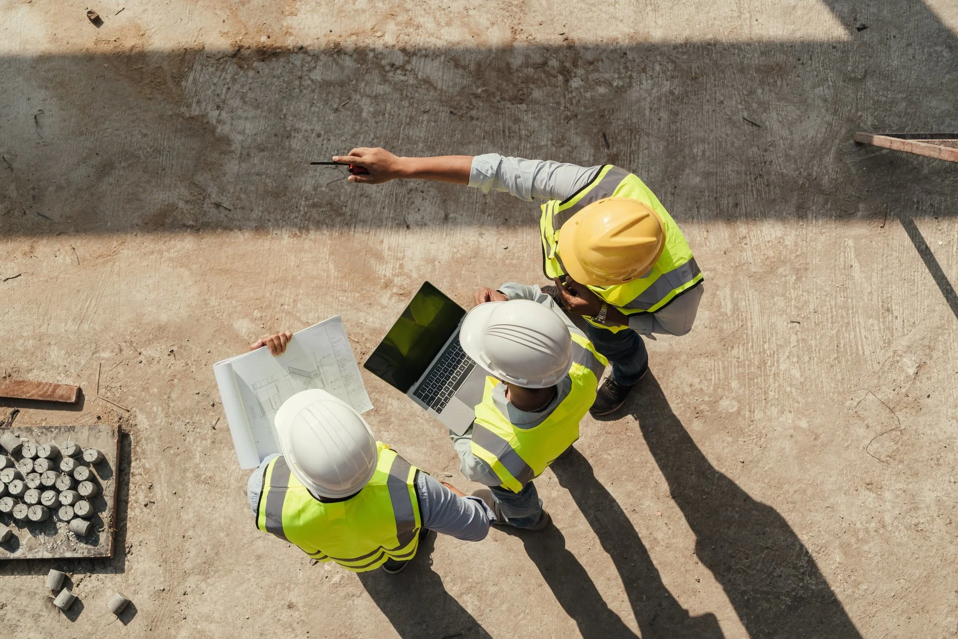 Three workers on a construction site, in high visibility vests, reviewing plans together