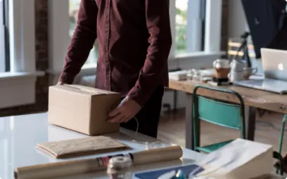 A small business owner packs stock into a cardboard box for delivery.